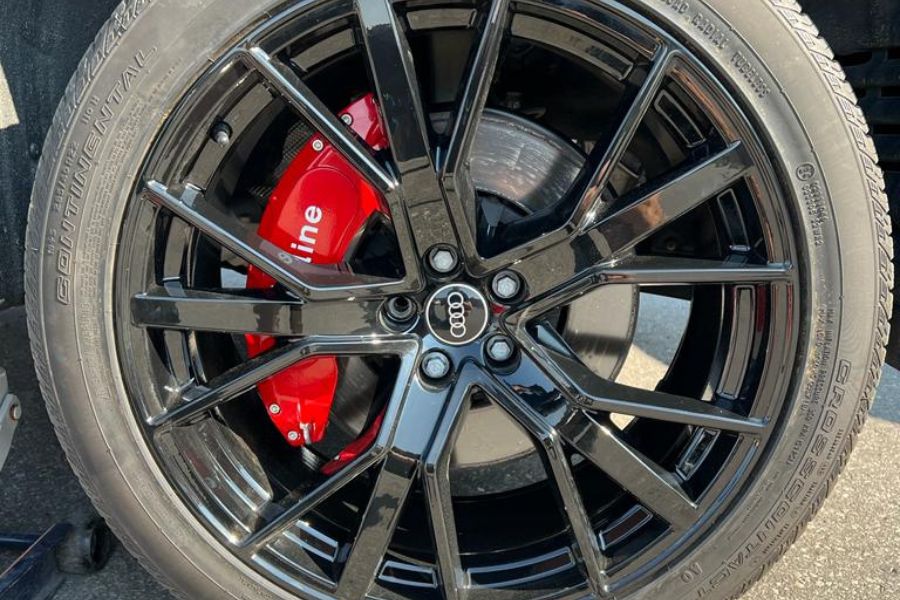 A black custom caliper cover on an Audi vehicle's wheel, featuring a red brake caliper and the Audi logo on the center of the wheel.