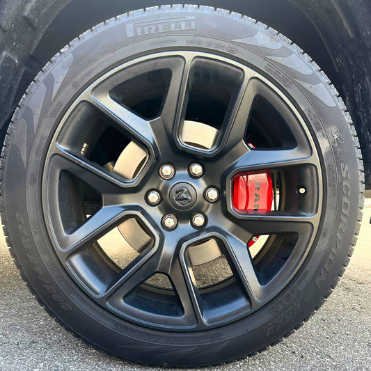 Close-up of a car wheel with a visible brand logo on a Leprecon Plus caliper cover on a pavement background