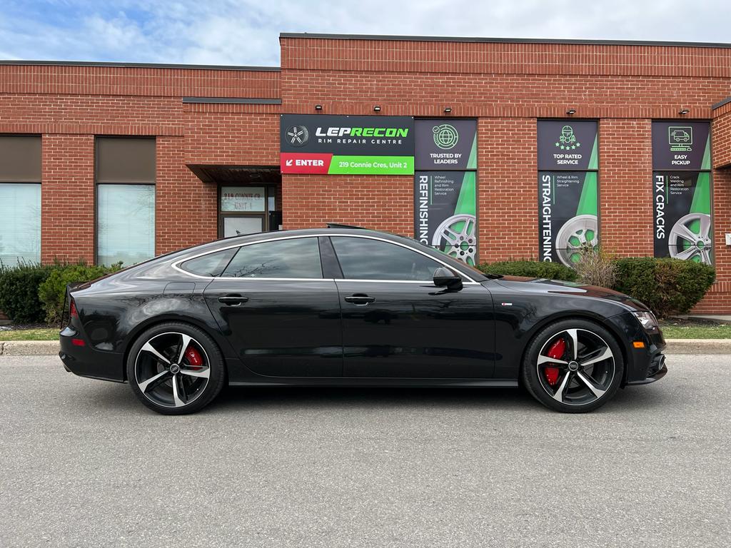 Black Audi A7 parked in front of a brick building with Leprecon automotive signs.