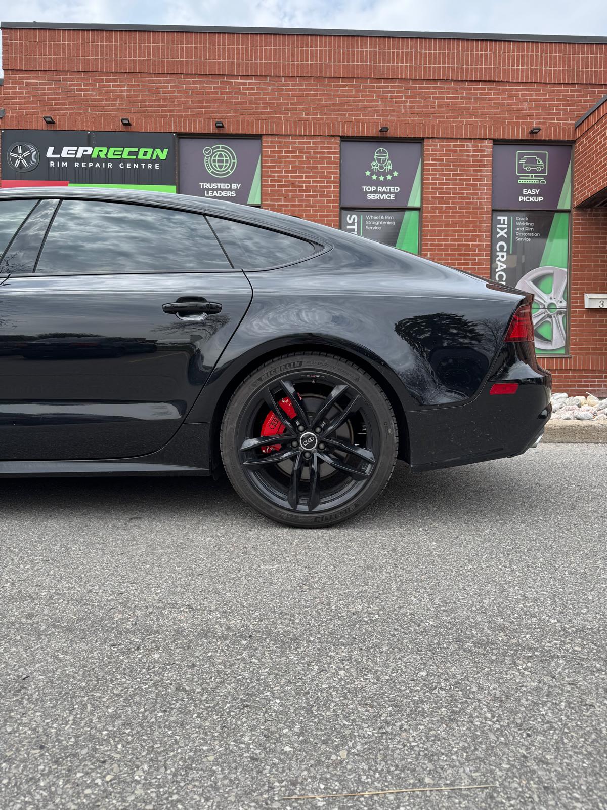 Black Audi A7 parked in front of a brick building with Leprecon branding.