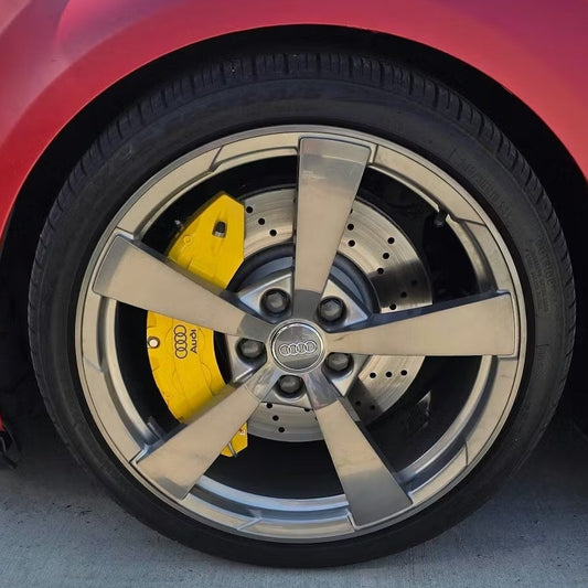 Close-up of a red Audi A3 wheel with a yellow hubcap on a concrete surface.