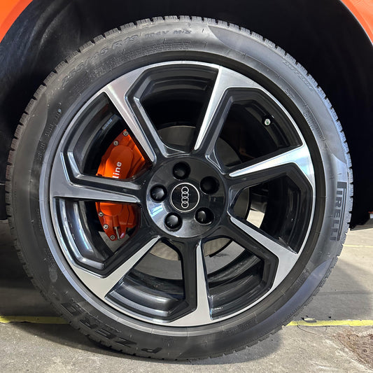 Close-up of an Audi Q3 wheel with orange brake caliper on a black tire.