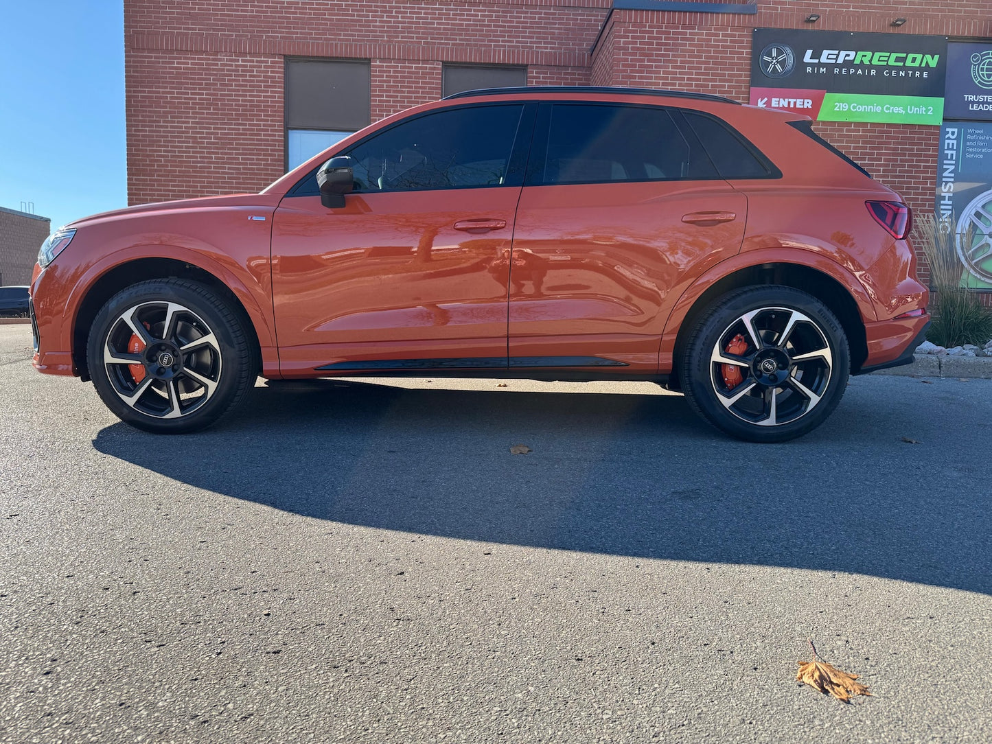 Orange SUV Audi Q3 parked in front of a brick building with signs.