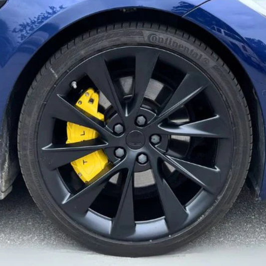 Close-up of a Tesla S wheel with a black rim and yellow brake caliper on a blue car.